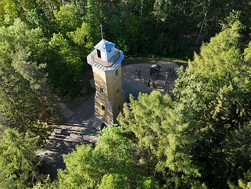 Der Perlaser Turm von oben, umgeben von Wald mit einem Spielplatz dahinter